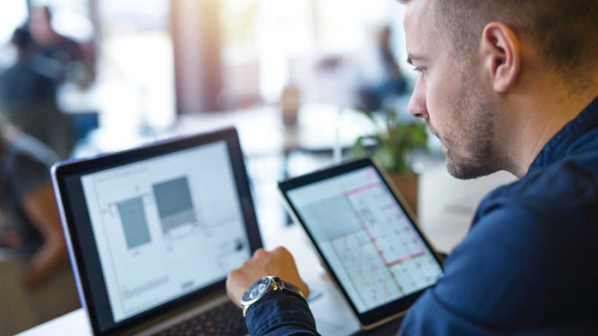 Profissional analisando dados em laptop e tablet em ambiente corporativo